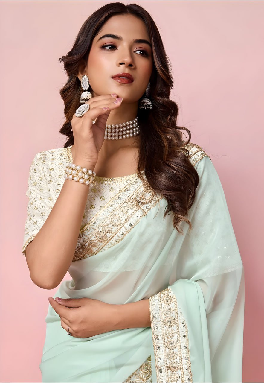 Woman wearing a light blue saree with gold embroidery on a pink background
